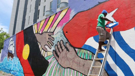 Aktivis pembebasan Papua Barat Piter Elaby memberikan sapuan akhir mural di pusat kota Darwin pada Australia Day 2016 lalu.  ABC News: Felicity James
